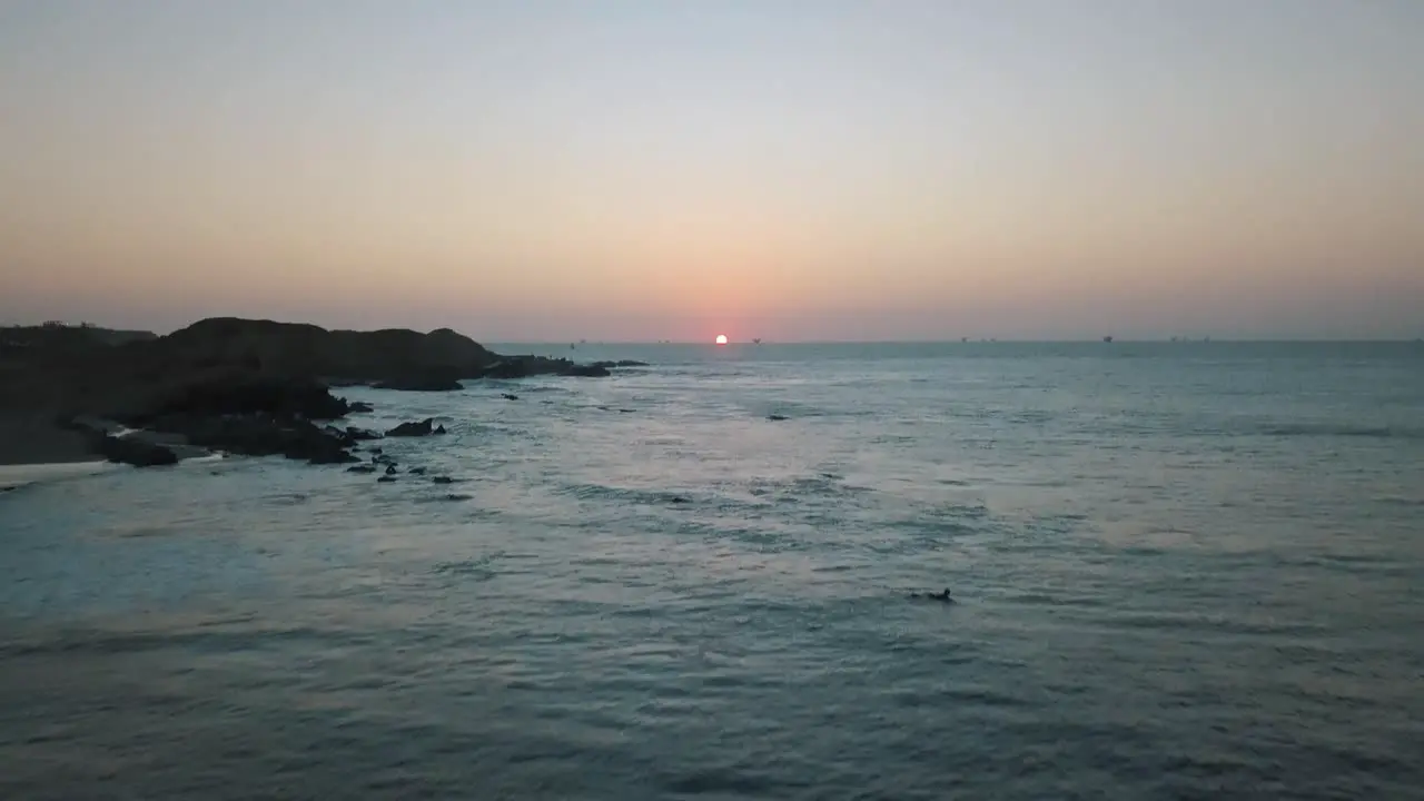 Aerial forward tilt up reveal of surfers on surfboards waiting for wave at sunset