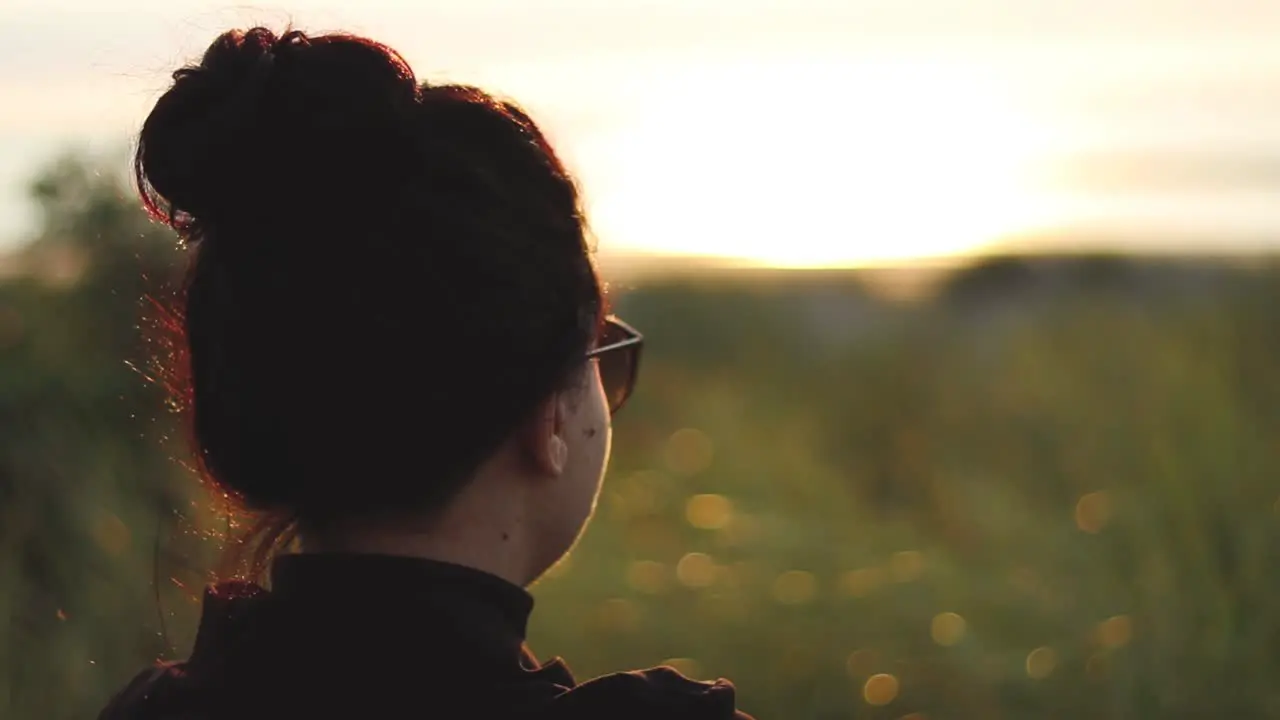 Girl with sunglasses watching the sunset by the the ocean sitting on a bench