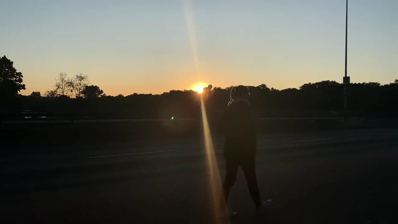 Silhouette of blonde young pretty woman walking down the street in front of the sun going down