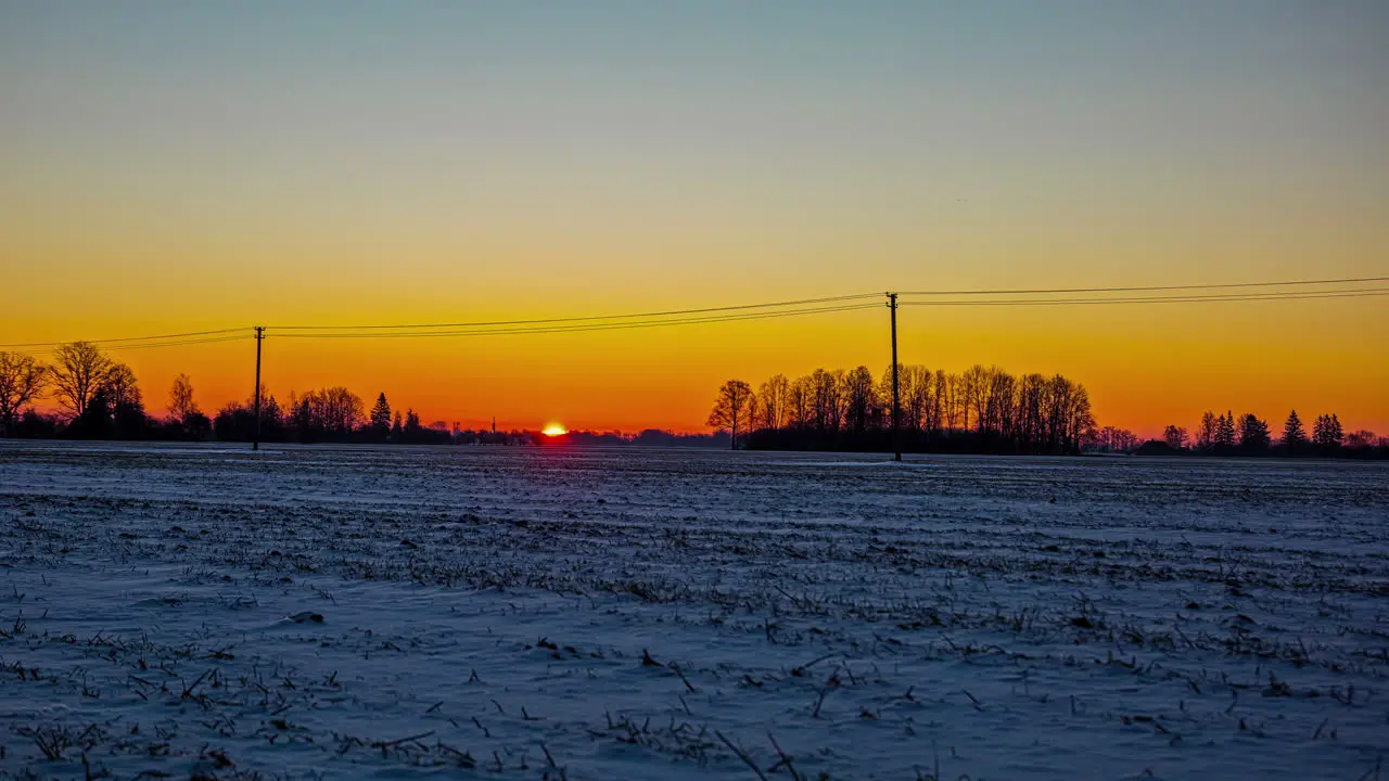 At sunrise the fiery sun rises above the horizon and illuminates the snowy European countryside time lapse