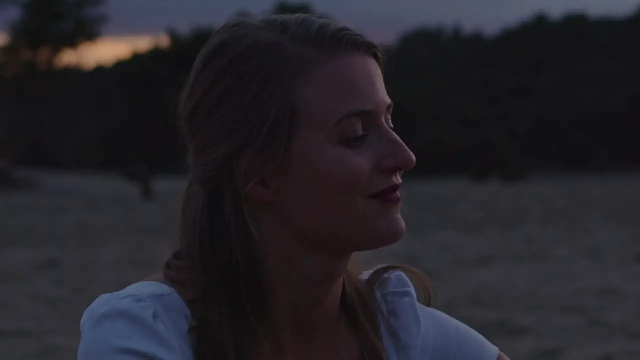 Close up of attractive young woman sitting in sand dunes at dusk