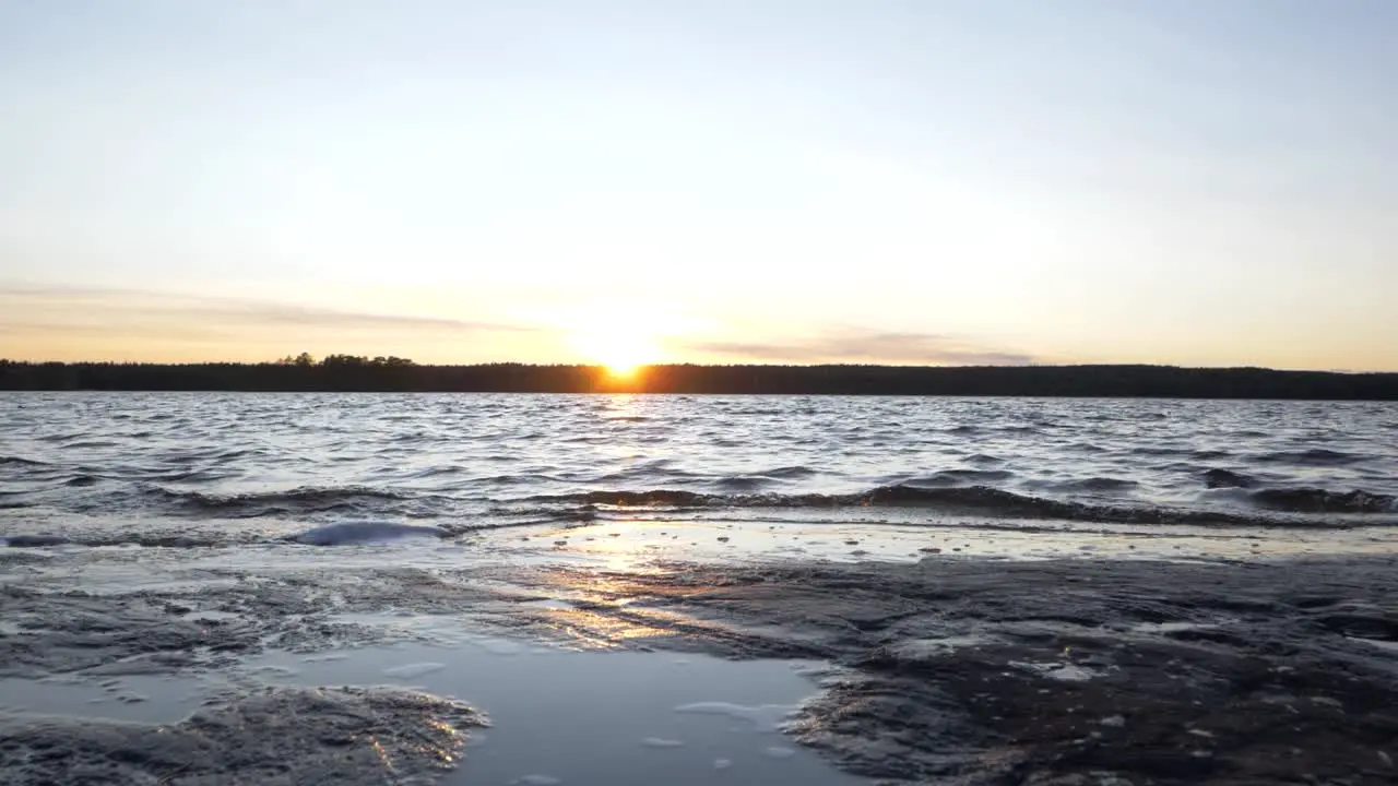 Low Angle push in Shot Of Beach At Dusk With Waves Washing Up Slowly On the Shore While The Shot Cranes up Revealing a Majestic Sun Setting in the Horizon