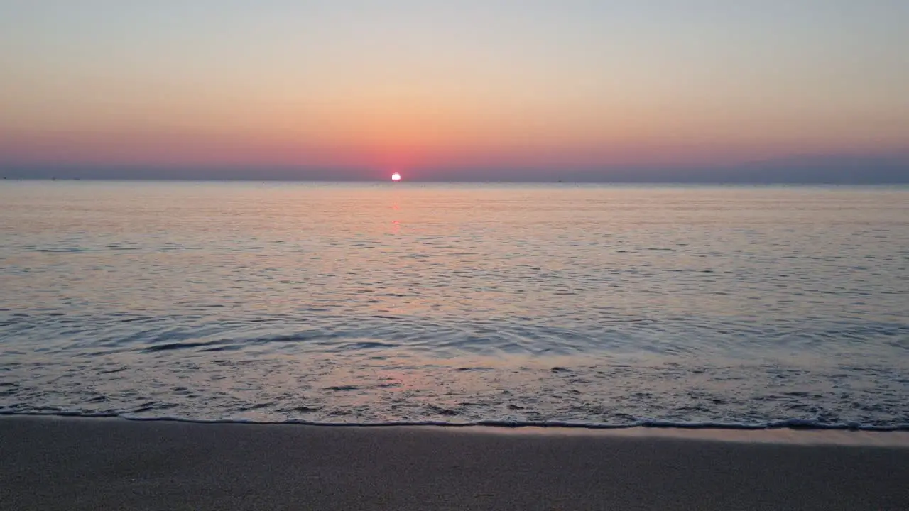 Calm water surface and sea waves splash on sandy beach at sunrise