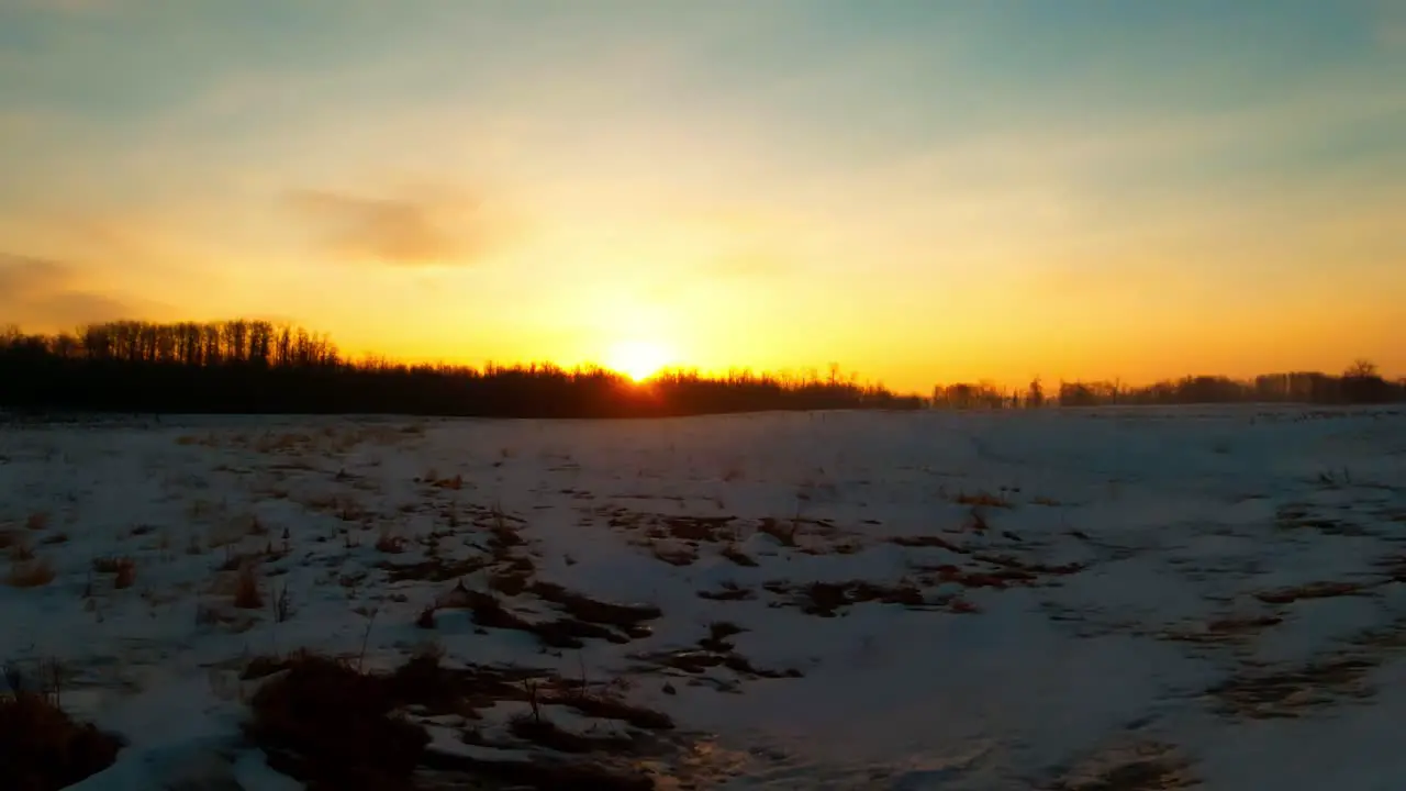 The Sunrises glows in center view in a winter horizon melt down as the reflection has an amber lighting spreading from the middle frame to the bottom while clouds above dissipate in time lapse motion