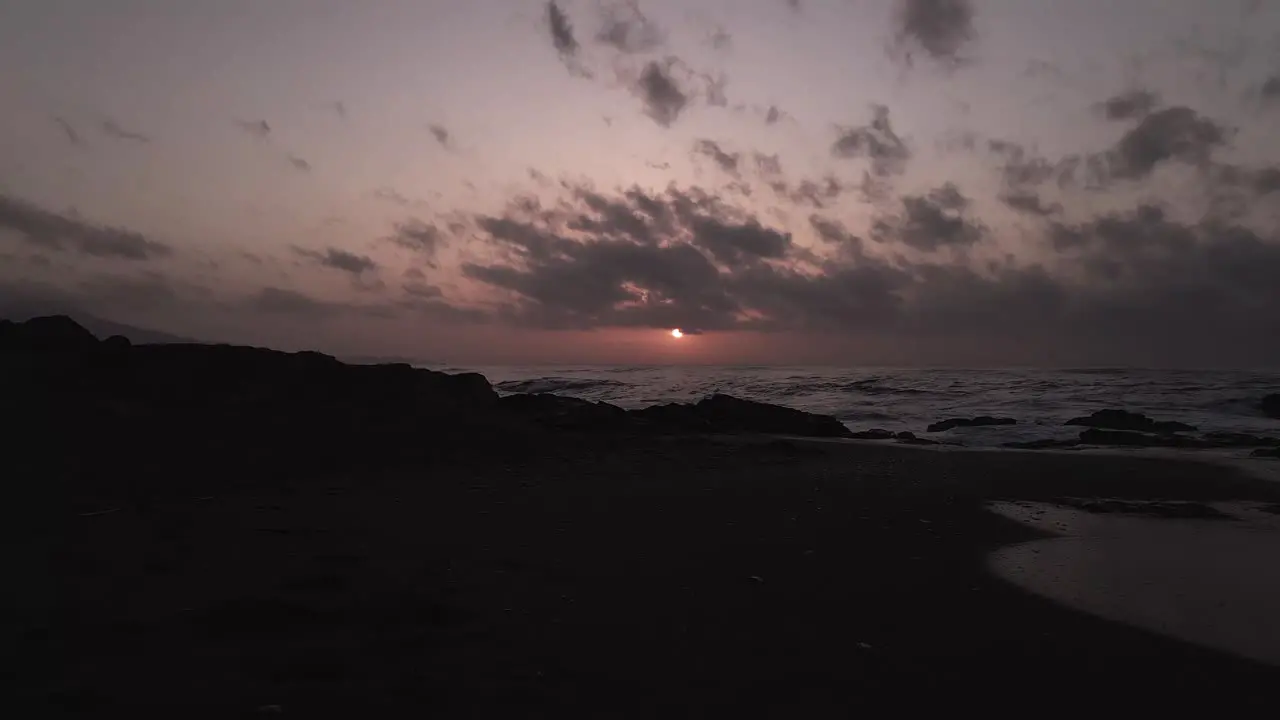 Aerial view descending to sunset silhouette coastal rocky beach ocean waves seascape horizon