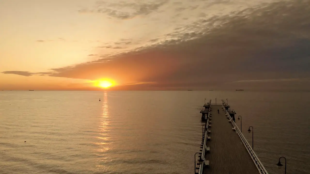 Smooth aerial drone flying over the sea towards the sun next to the wood boardwalk