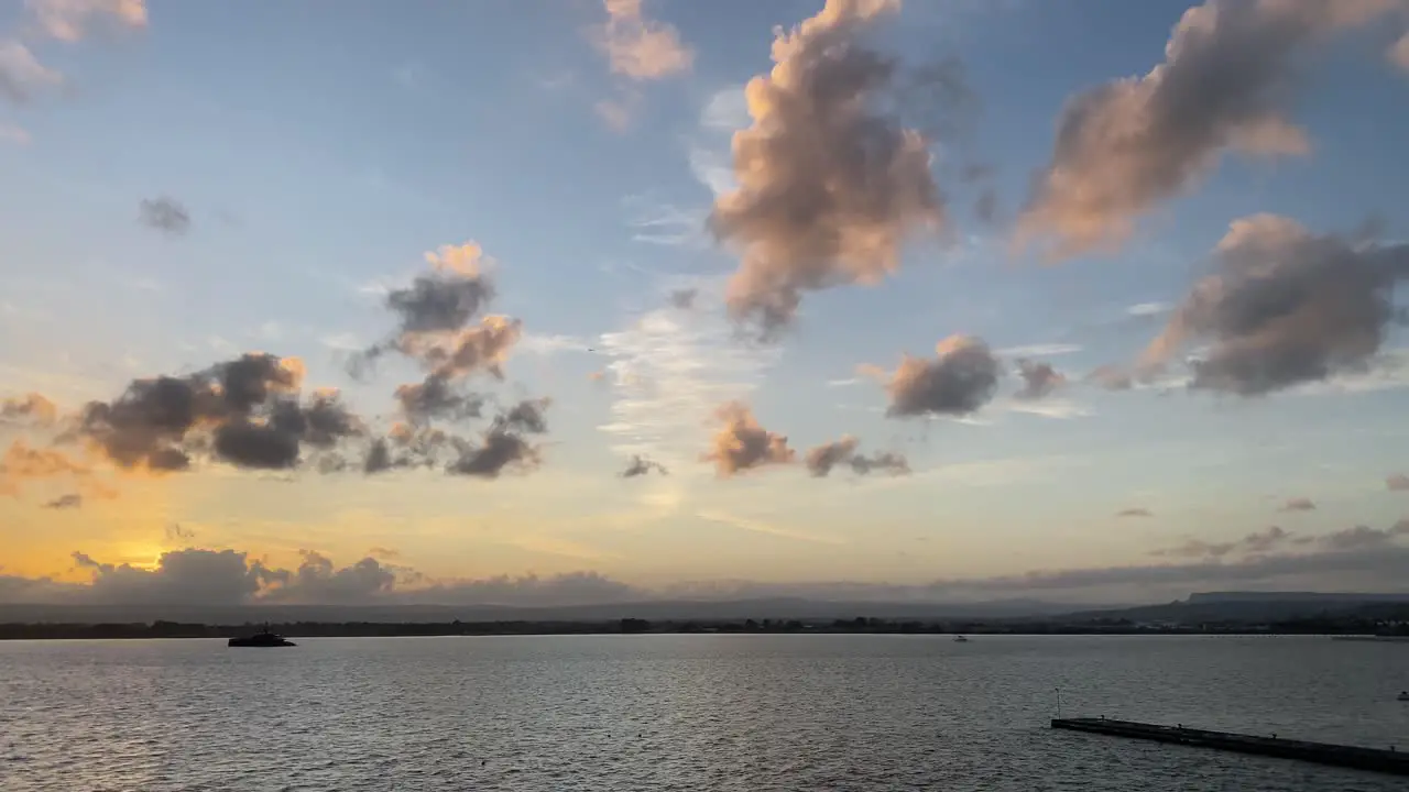 Dreamy sunrise with colorful clouds over calm rippled water static shot