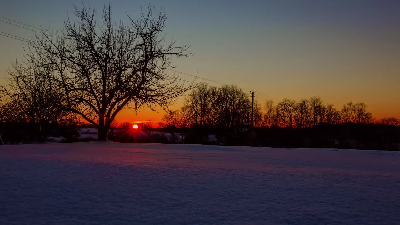 Brilliant orange sunset on a winter day over European snowy countryside time lapse