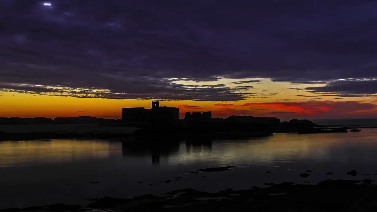 timelapse at a beautiful orange sunset on the edge of a lake with silhouettes of buildings in the background