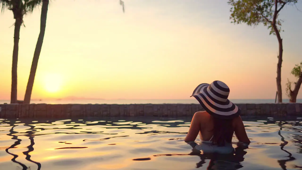 Solitary Female Standing in Pool With Summer Hat and Enjoying the View on Sunset Sunlight Over Tropical Sea