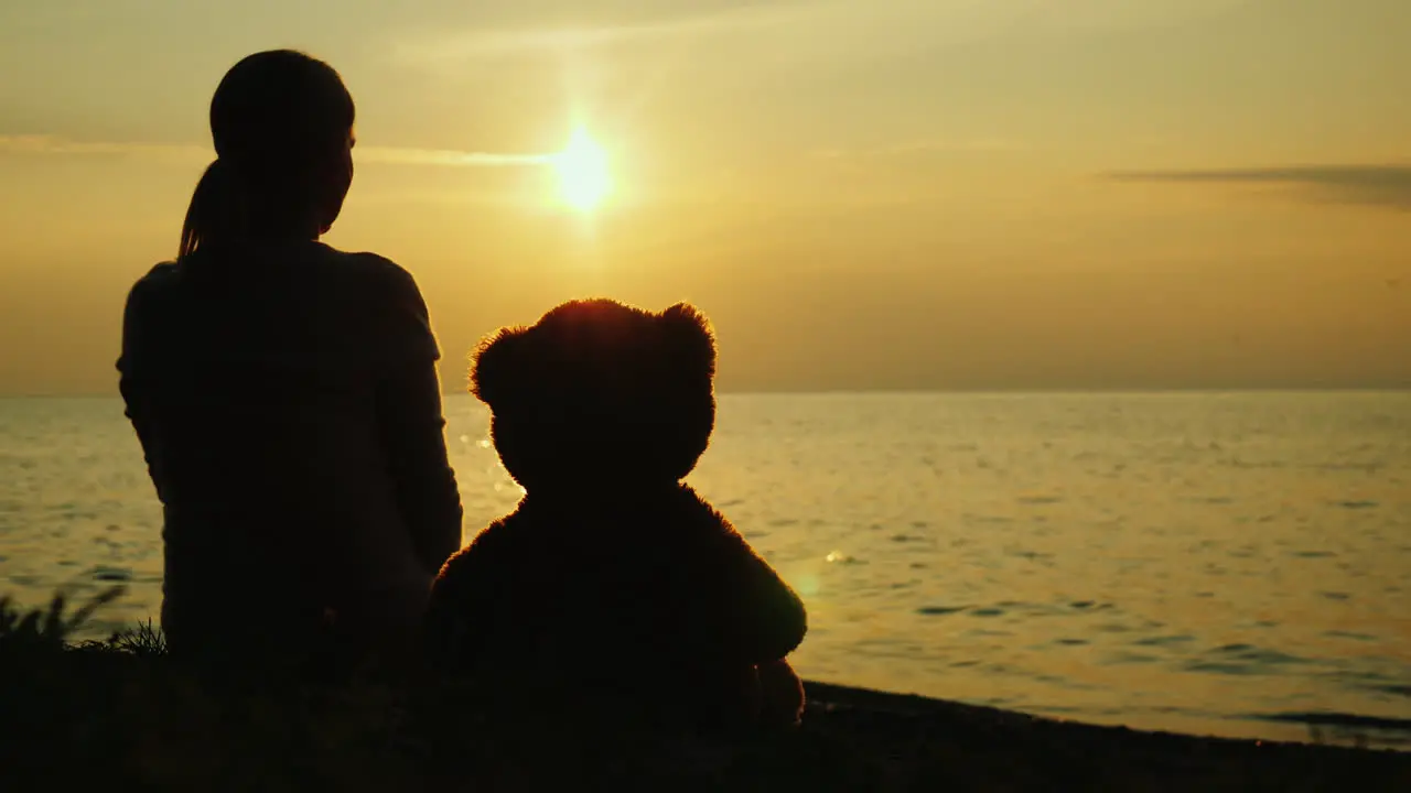 A Lonely Woman With A Toy Bear Looks At The Sunset Over The Sea Sadness And Loneliness Concept