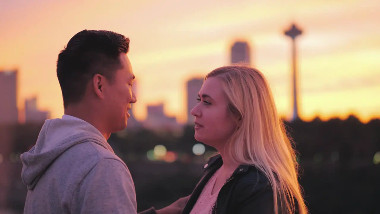 Multiethnic Young Couple Talking On The Bridge Against The Backdrop Of A Big City And A Beautiful Su