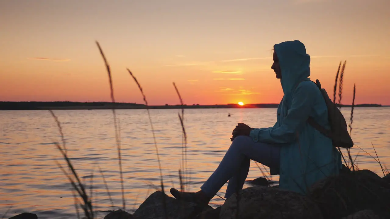 Woman Sits On A Rock Near A Picturesque Lake At Sunset