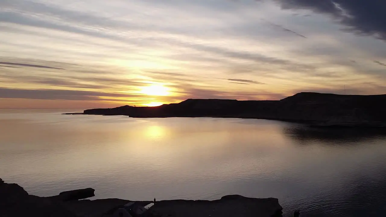 Lonely Young Man Sitting On A Mountain Ledge Looking To The Sea With Golden Sunset Aerial Zoom-In Shot