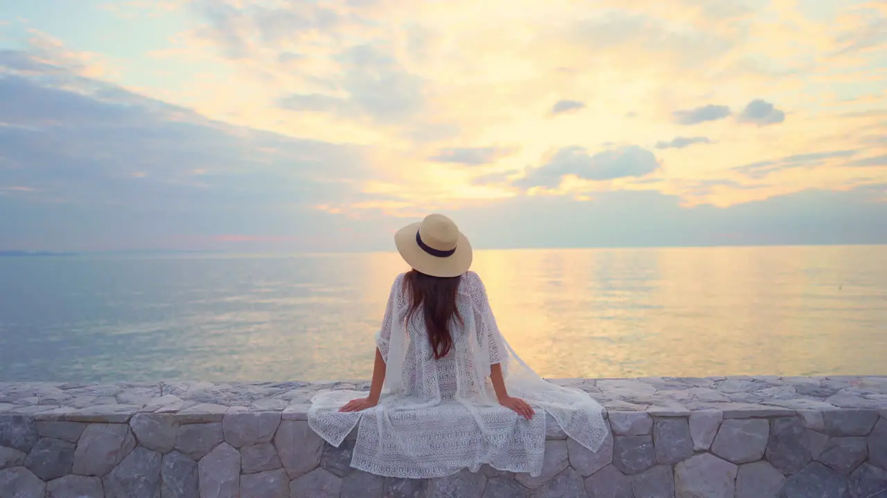 Back view of a woman admiring a spectacular sunset with cloudy dramatic sky and colourful reflection on the ocean