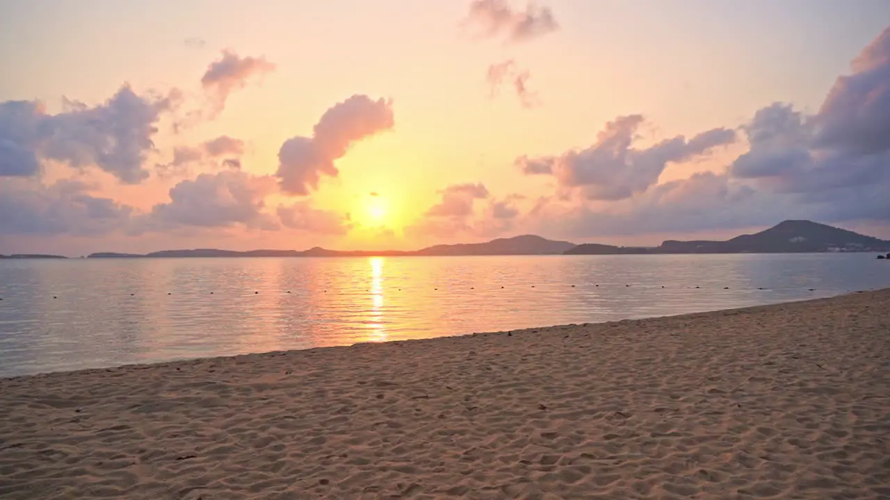 A view from the beach of a cloudscape forming around the mountains reflecting the pink purple and yellow tropical setting sun