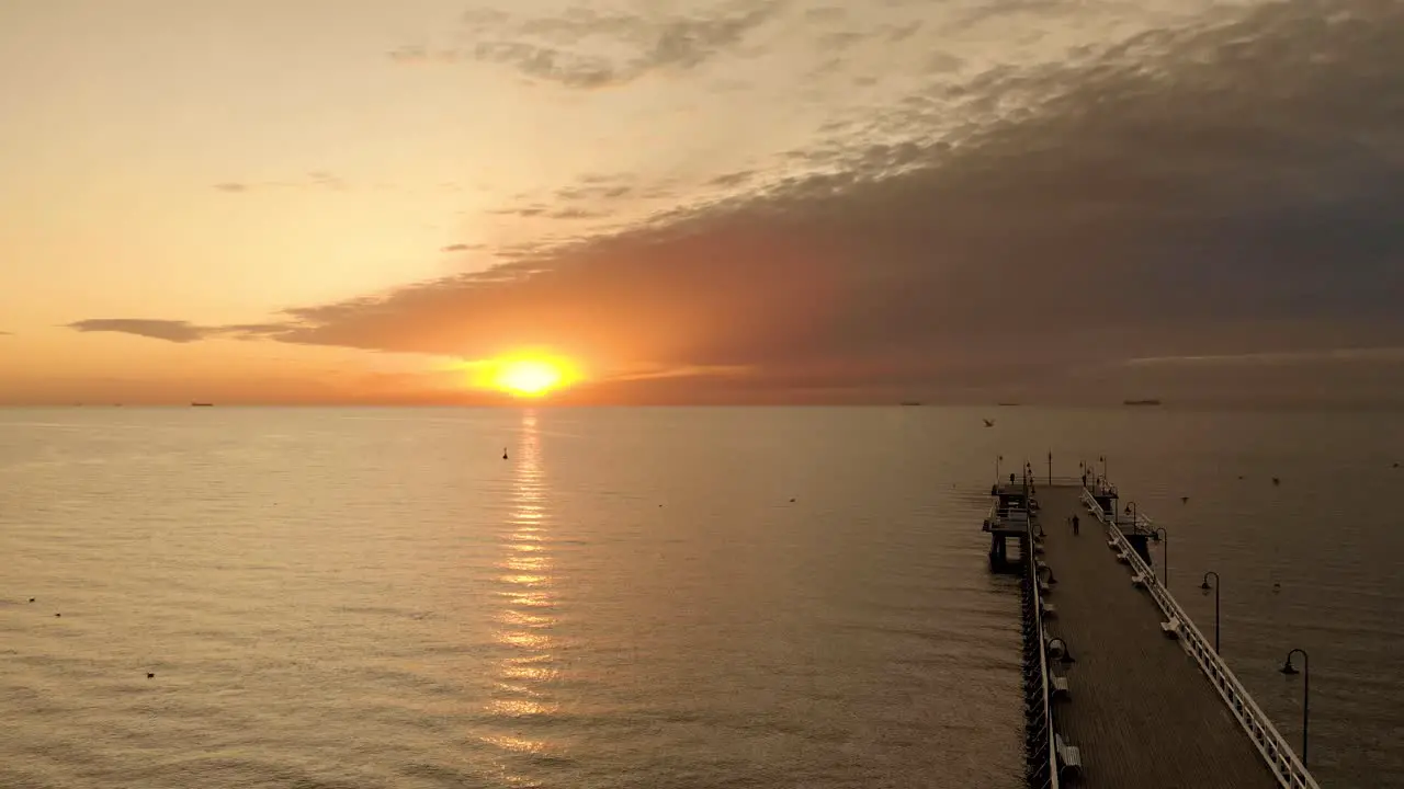 Beautiful aerial flight over the baltic sea and a wooden boardwalk with people while sunrise in the morning