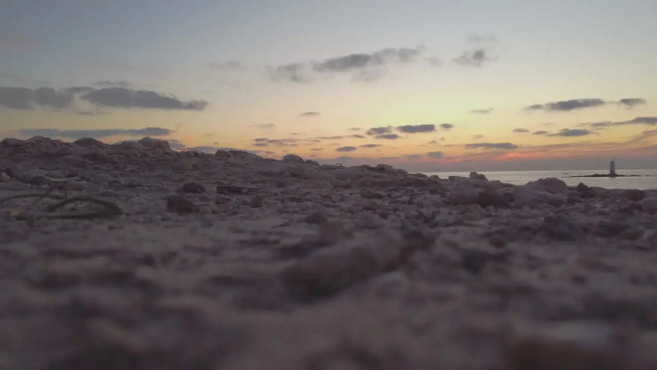 Low static shot of ground terrain with offshore lighthouse on background sunset