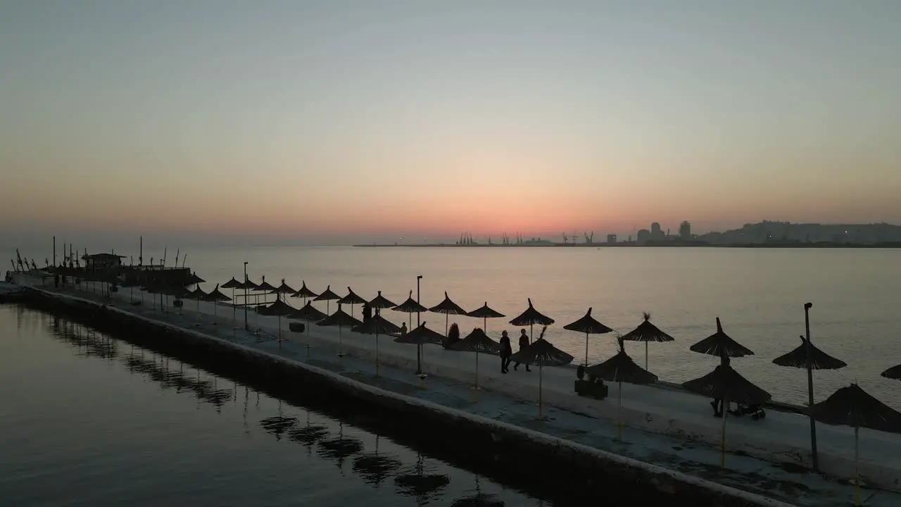 Silhouette people stroll on Durres jetty at dusk with Port on horizon