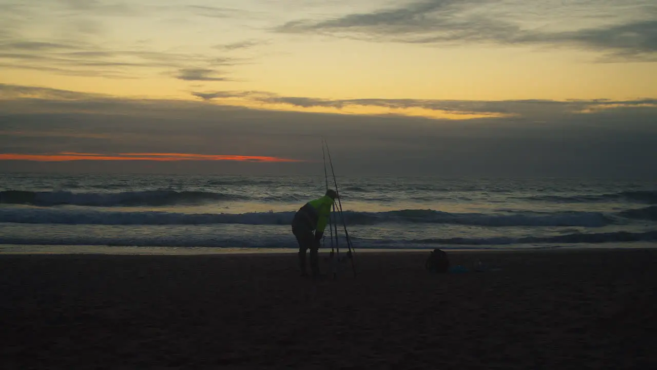 Silhouetted Man Fishing At Holywell Bay Beach At Sunset In England