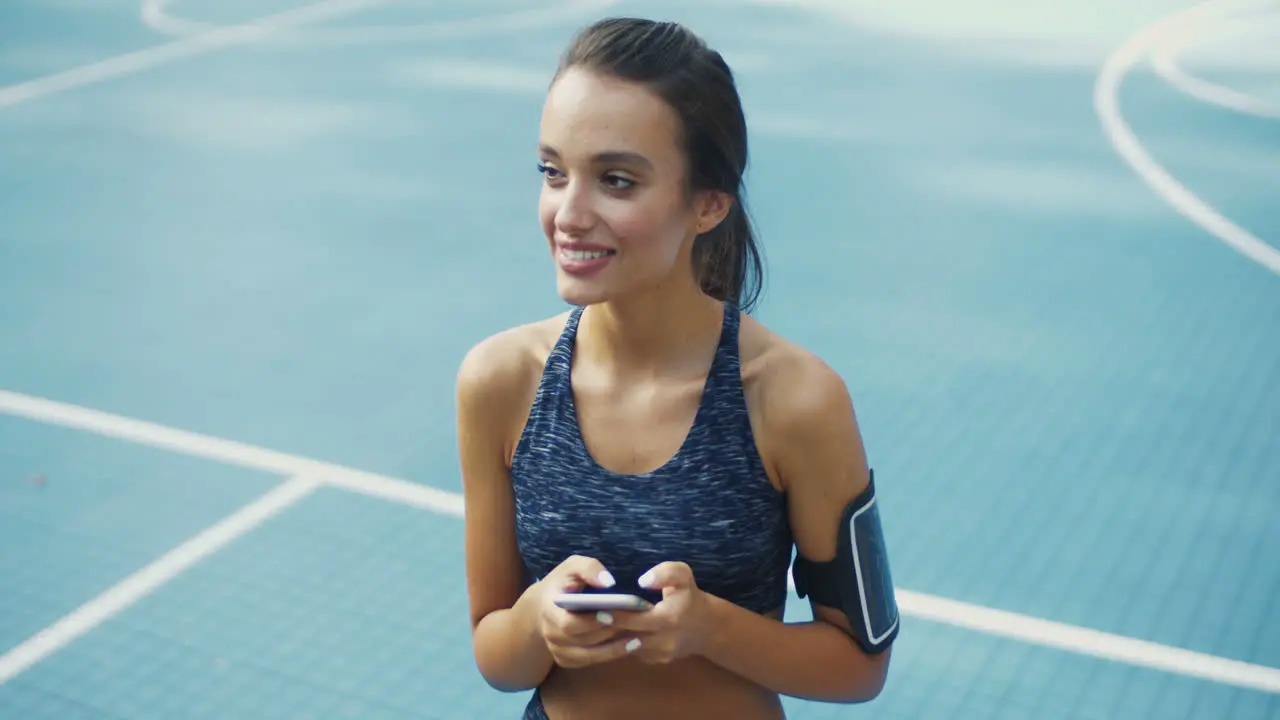 Sporty Girl With Airpods Laughing While Texting Message On Smartphone At Outdoor Court On A Summer Day 2