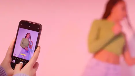 Studio Shot Of Woman Taking Photo Of Friend Dancing On Mobile Phone Against Pink Background 3