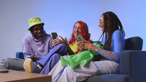 Studio Shot Of Group Of Young Gen Z Friends Sitting On Sofa Gaming And Using Social Media On Mobile Phones 2