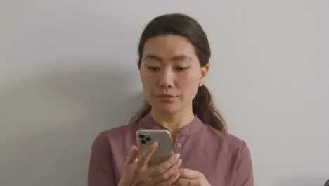 Nervous Female Candidate Wearing Suit In Office Waiting For Job Interview Looking At Mobile Phone 