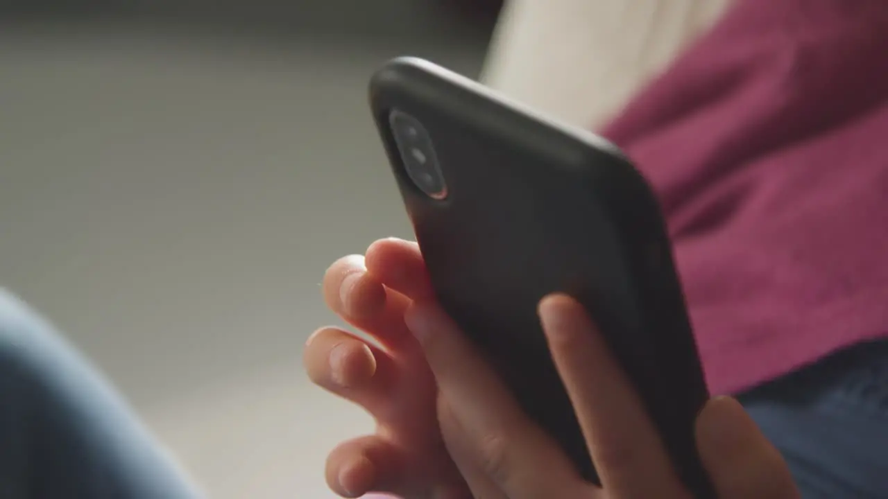 Close Up Of Girl Sitting On Sofa At Home Looking Online Using Mobile Phone 5