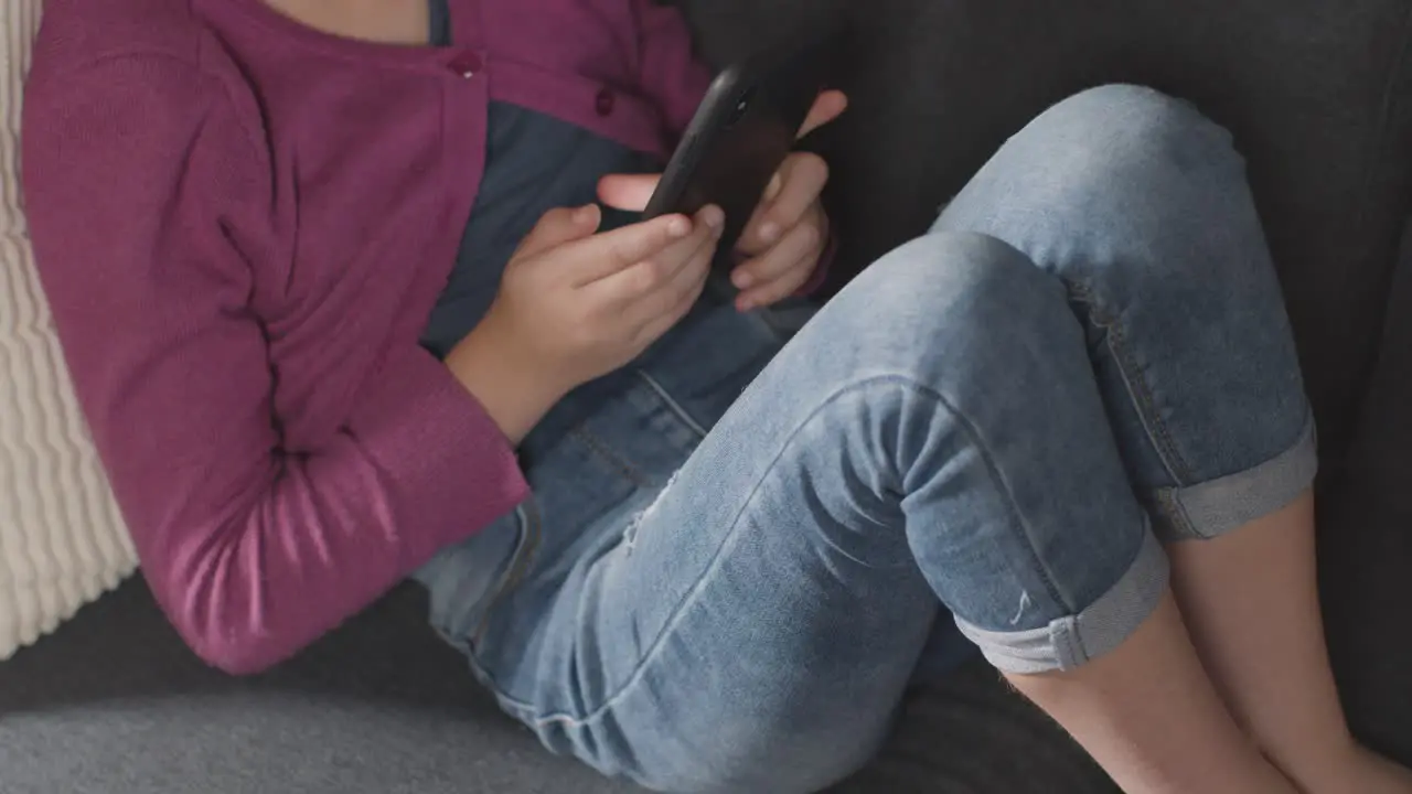 Close Up Of Girl Sitting On Sofa At Home Looking Online Using Mobile Phone 3