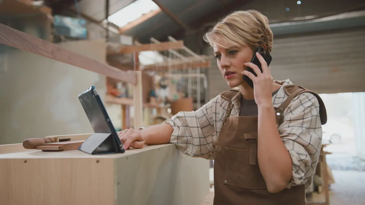 Frustrated Female Carpenter With Digital Tablet Working In Furniture Workshop Making Phone Call