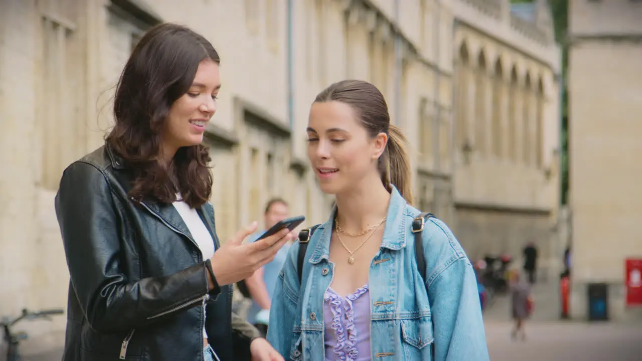 Same Sex Female Couple Sightseeing Follow Map App On Mobile Phone As They Walk Around Oxford UK