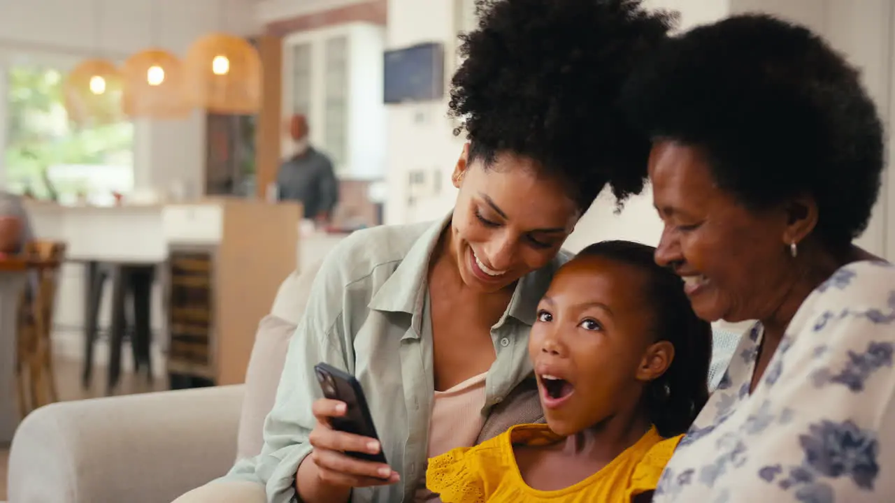 Multi-Generation Female Family Looking At Social Media On Mobile Phone Sitting On Sofa At Home Together