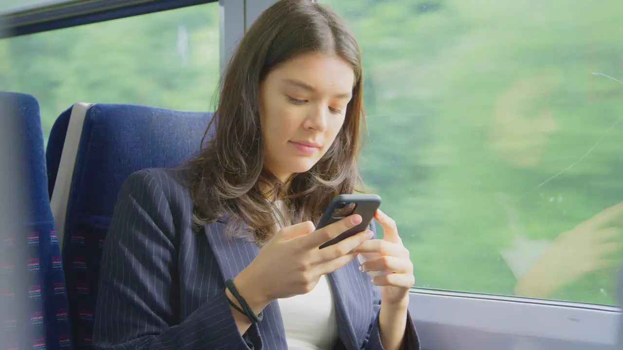 Businesswoman With Wireless Earbuds Commuting To Work On Train Looking At Mobile Phone