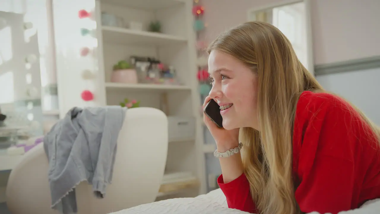 Teenage girl wearing orthodontic braces lying on bed at home talking on mobile phone and smiling shot in slow motion