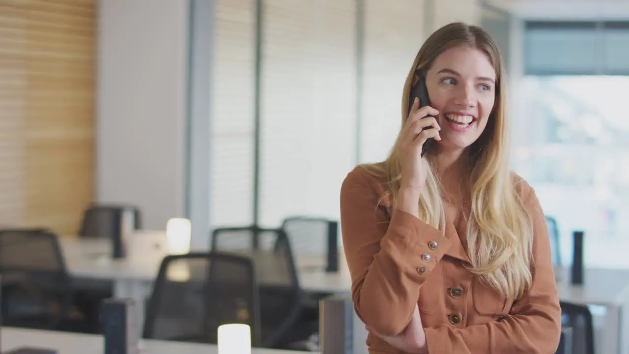 Smiling Businesswoman On Phone Call Standing In Modern Open Plan Office