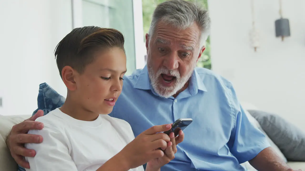 Hispanic Grandson Showing Grandfather How To Use Mobile Phone At Home