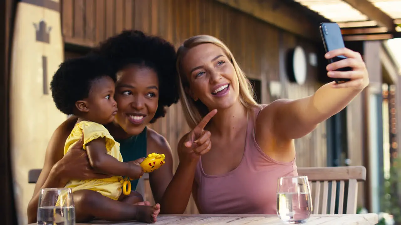 Same Sex Family With Two Mums Taking Selfie With Young Daughter Outdoors At Home