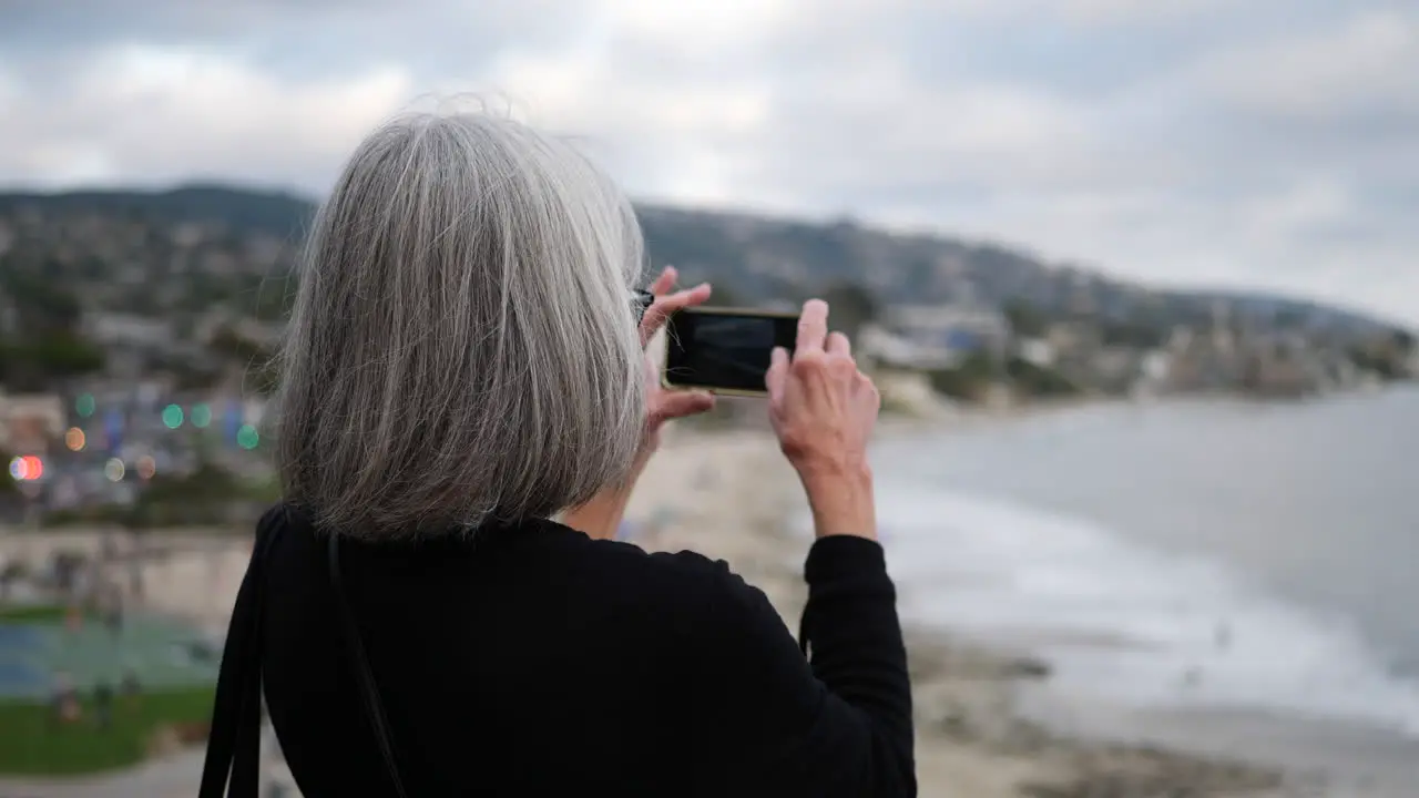 A middle aged woman on vacation taking a picture with her phone of the city and ocean in Laguna Beach California SLOW MOTION