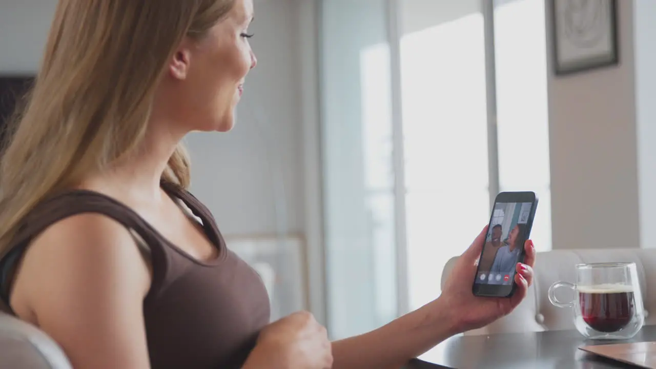 Pregnant Woman With Mobile Phone Making Video Call To Friends At Home Holding Stomach