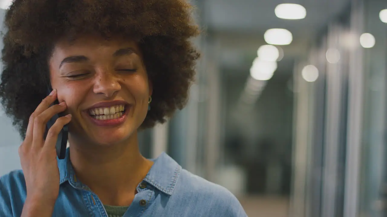 Smiling Businesswoman Standing In Corridor Of Modern Office Talking On Mobile Phone