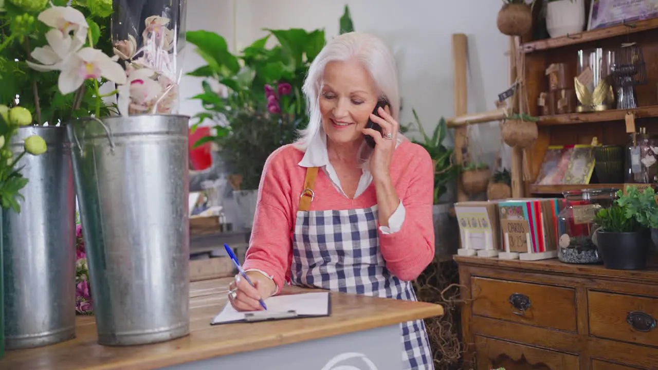 Female Owner Of Florists Shop With Clipboard Taking Order Over Phone