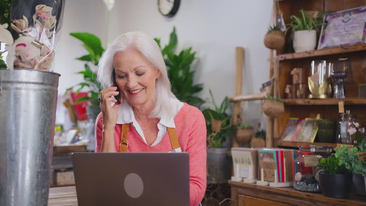 Female Owner Of Florists Shop With Laptop Talking On Mobile Phone