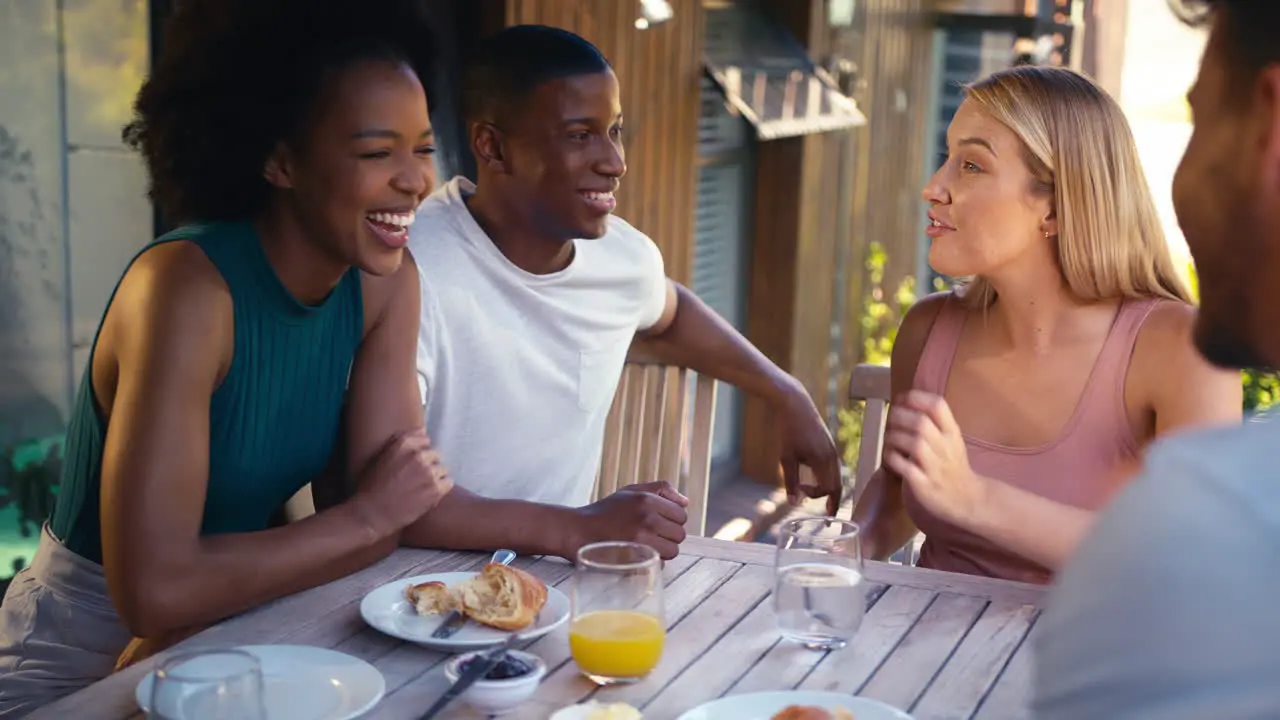 Group Of Smiling Multi-Cultural Friends Eating Breakfast Outdoors At Home Looking At Mobile Phone