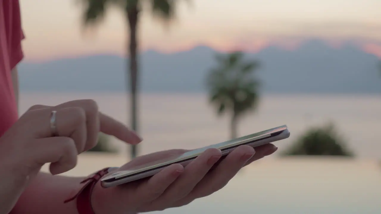 A closeup of female hands tapping a message on a smartphone screen against summer scenery