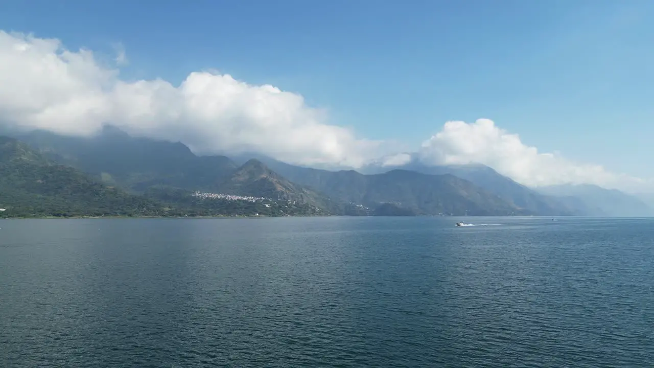 Drone view in Guatemala flying over a blue lake surrounded by green mountains approaching a moving boat on a sunny day in Atitlan