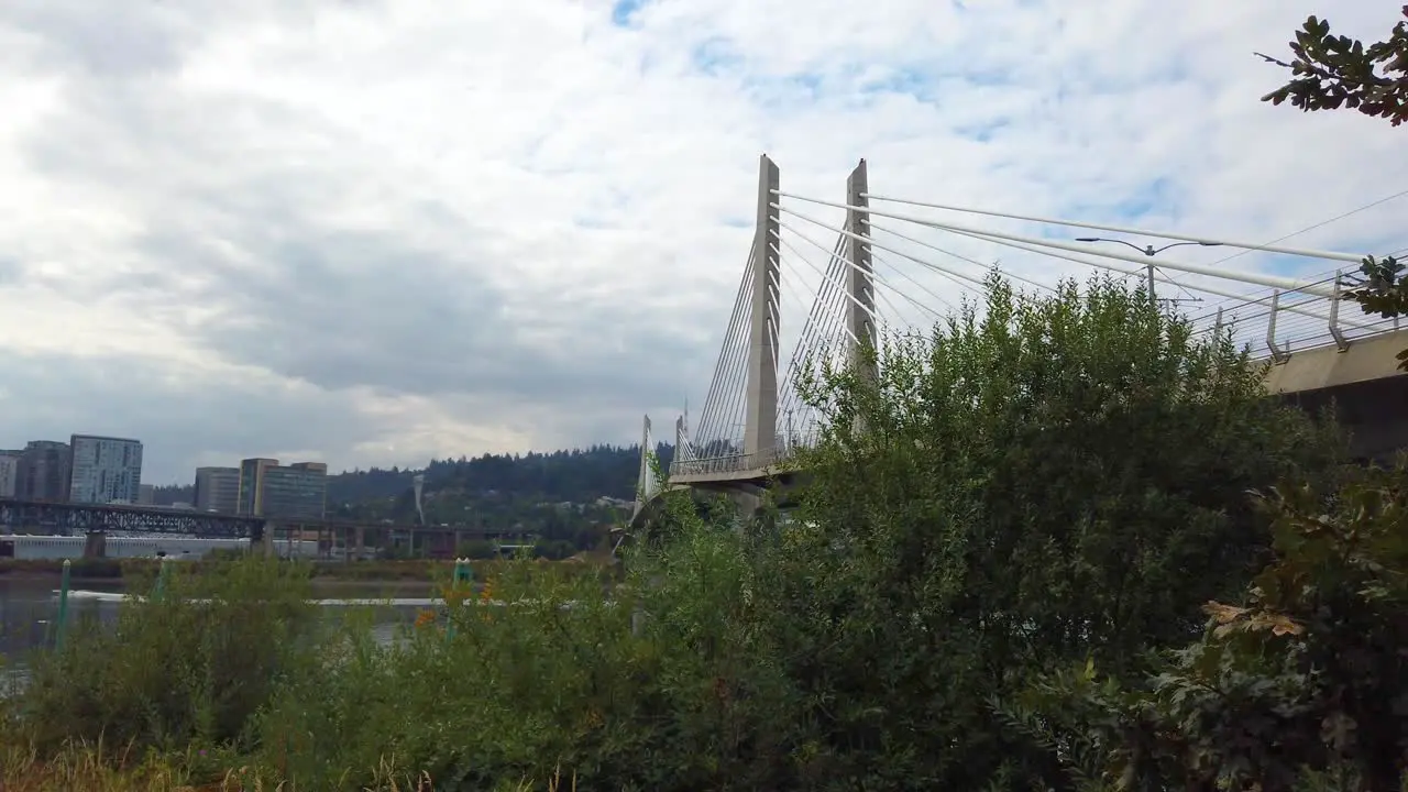 4K Portland Oregon trucking right to left from behind trees reveal of Tilikum Crossing Bridge over Willamette River with mostly cloudy sky