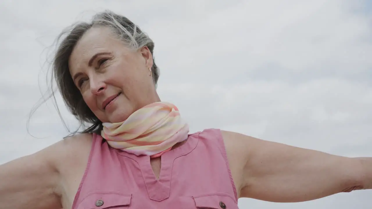 Happy senior caucasian woman with arms outstretched smiling against cloudy sky in slow motion