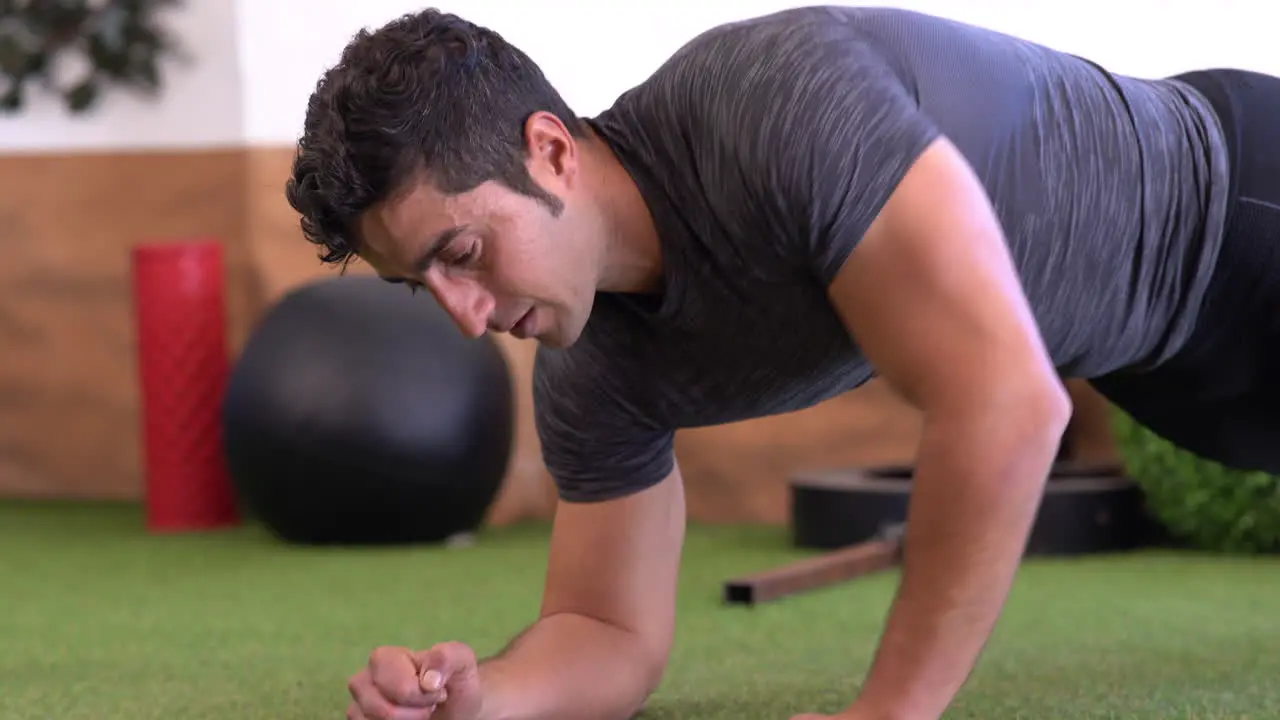 muscular trainer doing variations of plank exercise on gym grass floor