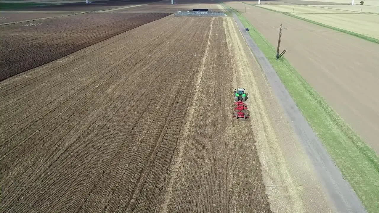 An aerial view at height of a tractor as it makes it's way down a field tilling the land to prepare it for the next crop